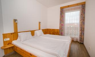 A simple, bright room with two single beds and wooden details. A large window provides plenty of daylight.