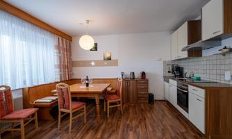 A cozy kitchen with a dining area and a large table. Bright furniture and large windows create a friendly atmosphere.