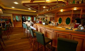 A cozy bar with wooden interior and green bar stools. In the background, friendly staff are serving guests.