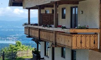 A cozy terrace with a wooden railing and blooming plants. In the background, there is a beautiful view of the valley and the mountains.
