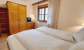 A cozy bedroom with two beds and a wooden wardrobe. The room has a window with curtains and a television.