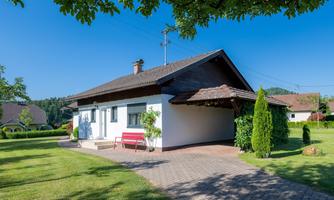 A beautiful single-family home with a large garden. The sky is clear and blue, surrounded by green trees.