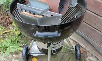 A grill with an open lid and a grill grate. Next to the grill is a chimney starter.