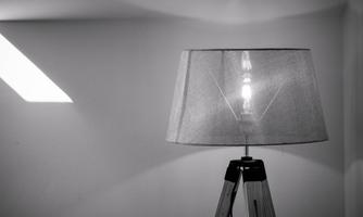 A modern floor lamp with a simple lampshade stands in a room. It emits warm light and creates a cozy atmosphere.