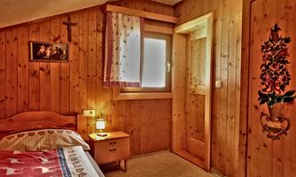 A cozy bedroom with wooden walls and a window. The room is simply furnished and has a warm atmosphere.