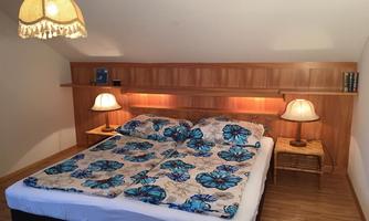A cozy bedroom with a double bed and colorful bed sheets. Against the walls are double nightstands with lamps and a wooden shelf.