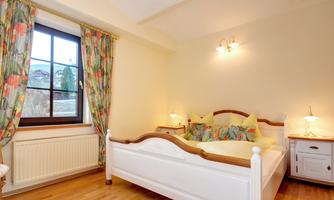 A cozy bedroom with a large bed and colorful curtains. The wooden floors give the room a warm atmosphere.