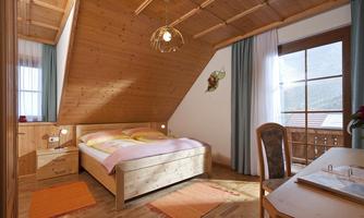 A cozy bedroom with wooden paneling and a large bed. The room has access to a balcony with a beautiful view.
