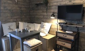 A cozy living area with wooden walls, a table, and a comfortable seating area. The room features a television and decorative elements.