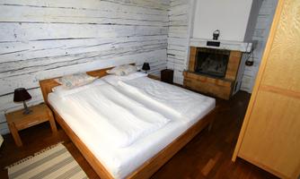 A cozy bedroom with a double bed and a fireplace. The walls are painted white and the floor is wooden.