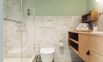 A modern bathroom with a glass shower and a wooden dresser. The walls are painted in neutral colors, and the tiles have a striking pattern.