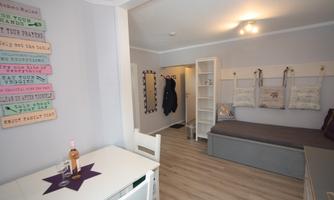 A cozy room with a bed and a small table. Decorative elements hang on the wall and a wardrobe is visible.
