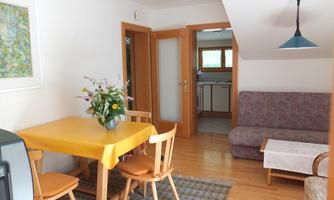A cozy living space with a dining table and chairs. In the background, a kitchenette and a sofa are visible.