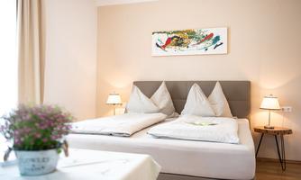 A modern bedroom with two beds and stylish cushions. A colorful piece of artwork hangs on the wall, and the light creates an inviting atmosphere.