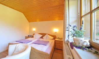 A cozy bedroom with two beds and a wooden ceiling. The windows provide plenty of natural light and a pleasant atmosphere.