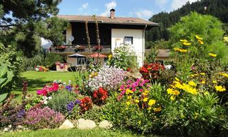 A beautiful house surrounded by a colorful garden with many flowers. The surroundings are green and mountainous, creating a tranquil atmosphere.