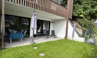 A cozy terrace with a table, chairs, and two loungers. The garden is green and well-maintained.