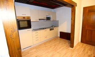 A modern kitchen with white cabinets and stainless steel appliances. The floor is made of light wood, and there is access to an adjacent room.