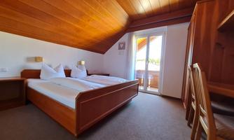 A cozy bedroom with two beds and a balcony. Bright wooden furniture and a warm wooden ceiling create an inviting atmosphere.