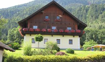 A traditional country house with blooming balcony flowers, surrounded by green landscapes and mountains. The scene radiates tranquility and a connection to nature.
