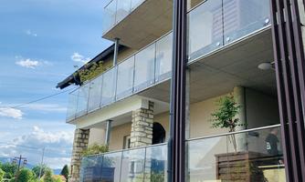 A modern building with several floors and glass balconies. The sky is clear and some plants are visible in the surroundings.
