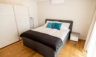 A modern bedroom with a cozy bed and colorful cushions. The room has bright walls and a warm wooden floor.
