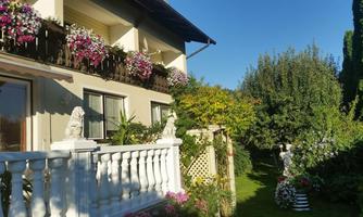 A charming house with a balcony adorned with colorful flowers. The garden is green and inviting, with decorative elements and plants.