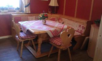 A cozy dining area with a wooden table and benches. The walls are painted red, and there are flowers on the table.