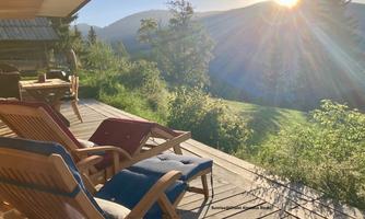 A terrace with two loungers and a table. In the background, the beautiful mountain landscape with the rising sun can be seen.