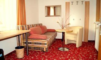A cozy living area with a sofa and a table. The walls are light, and the floor has a red carpet with a floral pattern.