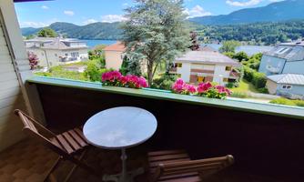 A balcony with a view of a picturesque landscape. The table and chairs are surrounded by colorful flowers.