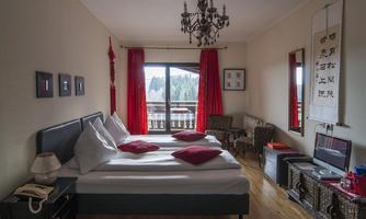 A cozy bedroom with a double bed and red accents.  
Windows with a view of nature and stylish furniture complement the space.