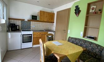 A cozy kitchen with wooden cabinets and a dining table. The walls are partially painted green, and there is a seating area with upholstered furniture.