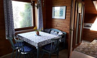 A cozy dining area with a table and wooden chairs. The windows offer a view of the outdoors, and the walls are paneled with wood.