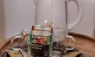 A kettle is on a table next to two glasses and tea bags. The set is prepared for a tea break.