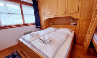 A cozy bedroom with wood paneling and a double bed. Fresh towels are ready, and large windows provide plenty of daylight.