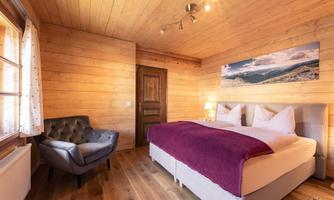 A cozy bedroom with wooden walls and a large bed. A comfortable corner with an armchair and a beautiful view of the mountains.