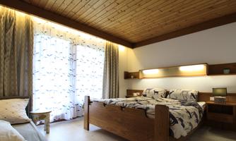 A cozy bedroom with a large bed and wooden furniture. The windows have curtains with a modern pattern and let in plenty of daylight.