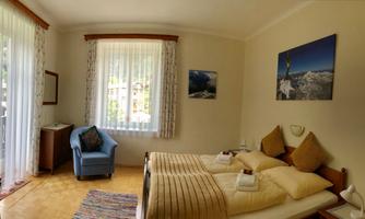 A cozy bedroom with two beds and light curtains. Pictures of mountains hang on the wall, and the room is furnished in a friendly and inviting way.