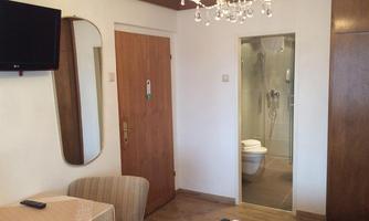 An elegant room with a large TV, a table, and a comfortable chair. In the background, there is a modern bathroom with a shower.