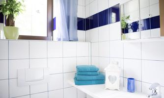 A modern bathroom with white tiles and blue accents. On the sink are freshly folded turquoise towels.