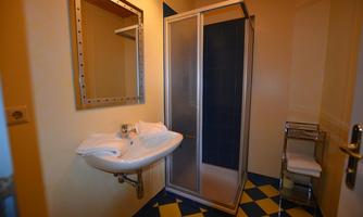 A bathroom with a shower and a sink. The walls are light, and the floor has a yellow and blue pattern.