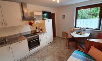 A modern, bright kitchen with white furniture and a small dining area. A window lets in plenty of light and offers a view of the greenery.