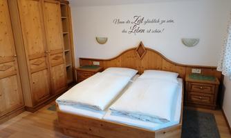 A cozy bedroom with a wooden double bed and light wood paneling. An inspiring quote is displayed on the wall.