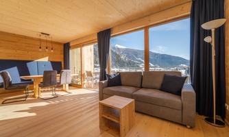 A bright and modern living kitchen with wooden paneling. Large windows offer a beautiful view of the mountains.