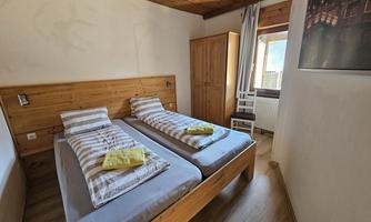 A cozy bedroom with two single beds and wooden details. The room has a window that lets in daylight.