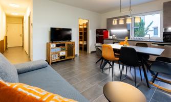 A modern living kitchen with a cozy sofa and a dining table. The room is bright and inviting, with a large window front.