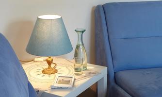 A cozy living area with blue sofas and a small table. On the table, there is a lamp, a water carafe, and a few decorative items.