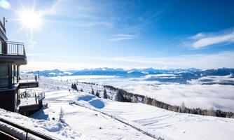 A snowy mountain landscape under a clear, blue sky. In the foreground, a ski pass and a viewing terrace can be seen.
