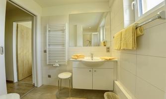 A modern bathroom with bright tiles and a large mirror. The amenities include a sink, towels, and a radiator.